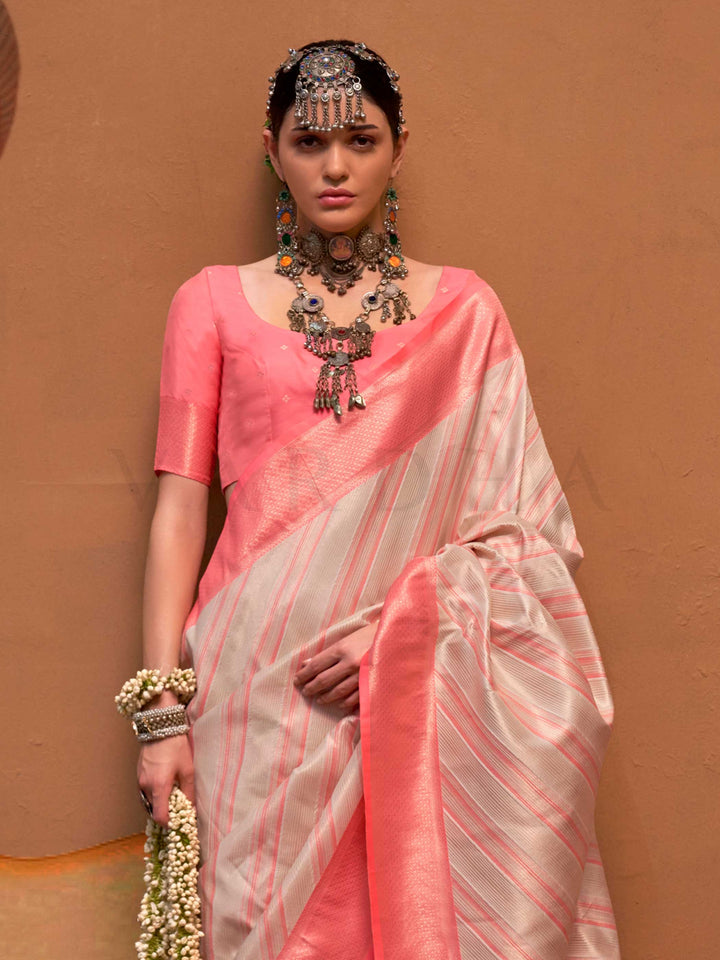 Ivory and Coral Pink striped silk saree with handloom weave and checked pallu. Ideal for wedding functions like bridal day pooja, styled with heritage jewelry and temple-inspired accessories. This image captures the side angle view showcasing blouse styling and zari border detail, ideal for visualizing festive elegance, designer appeal, and modern styling inspiration. Perfect for online shoppers seeking detailed previews before purchase, enhancing saree visual merchandising and SEO-rich product display stra