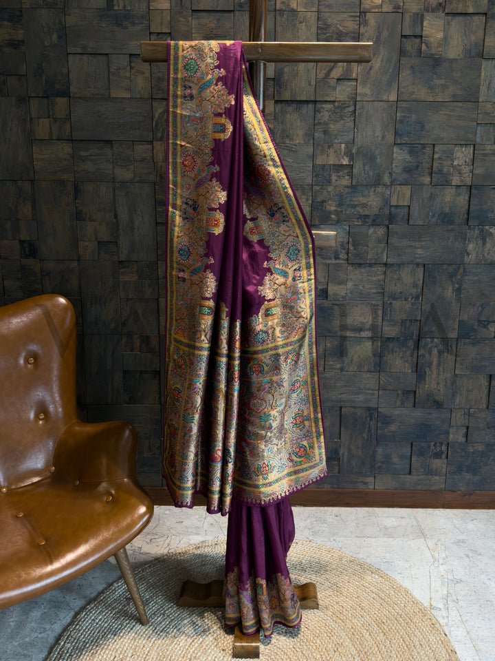 Traditional saree with intricate patterns draped over a wooden stand against a textured wall.