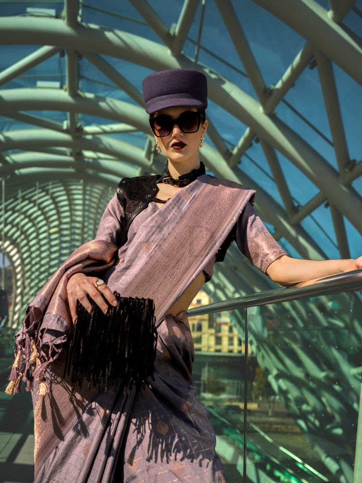 Dusty Lilac Katan silk saree with Rose Gold zari detailing, featuring checks handloom weaving, designer blouse and tasselled pallu — a perfect fit for party-wear and fashion walk. Styled with modern belts, hats, and accessories to blend heritage and couture elegance. This image captures the model styling perspective with complete saree ensemble displayed, ideal for visualizing festive elegance, designer appeal, and modern styling inspiration. Perfect for online shoppers seeking detailed previews before purc