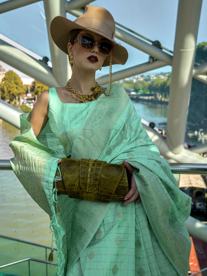 Mint Green Katan silk saree with Beige Gold zari detailing, featuring checks handloom weaving, designer blouse and tasselled pallu — a perfect fit for festive season and haldi ceremony. Styled with modern belts, hats, and accessories to blend heritage and couture elegance. This image captures the model styling perspective with complete saree ensemble displayed, ideal for visualizing festive elegance, designer appeal, and modern styling inspiration. Perfect for online shoppers seeking detailed previews befor