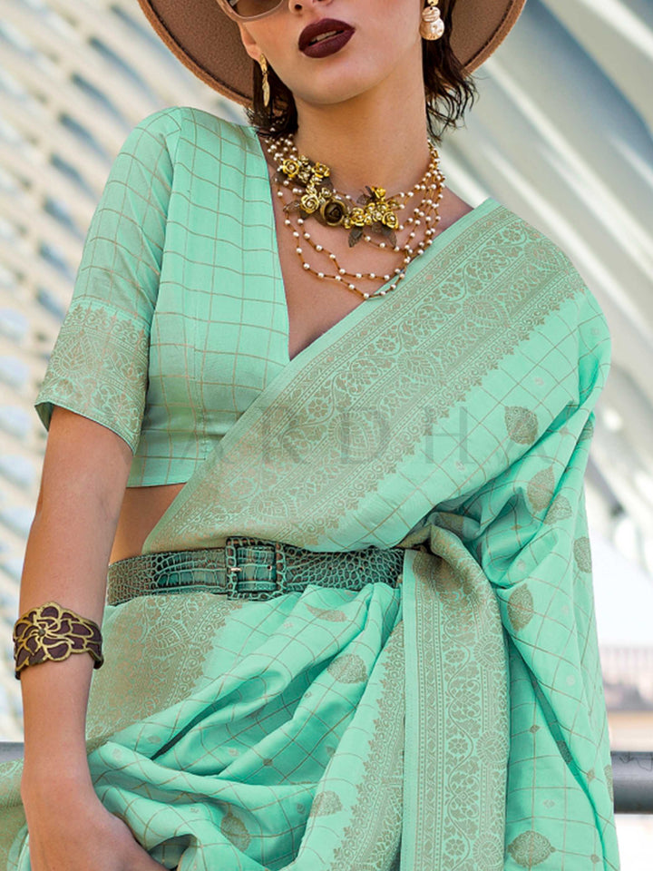 Mint Green Katan silk saree with Beige Gold zari detailing, featuring checks handloom weaving, designer blouse and tasselled pallu — a perfect fit for festive season and haldi ceremony. Styled with modern belts, hats, and accessories to blend heritage and couture elegance. This image captures the zoomed texture view illustrating fabric weave and print clarity, ideal for visualizing festive elegance, designer appeal, and modern styling inspiration. Perfect for online shoppers seeking detailed previews before