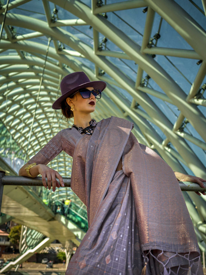 Grey Mauve Katan silk saree with Beige Gold zari detailing, featuring checks handloom weaving, designer blouse and tasselled pallu — a perfect fit for wedding and engagement function. Styled with modern belts, hats, and accessories to blend heritage and couture elegance. This image captures the model styling perspective with complete saree ensemble displayed, ideal for visualizing festive elegance, designer appeal, and modern styling inspiration. Perfect for online shoppers seeking detailed previews before