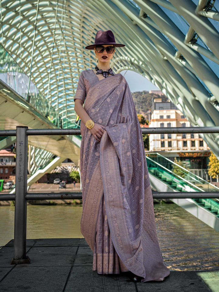 Grey Mauve Katan silk saree with Beige Gold zari detailing, featuring checks handloom weaving, designer blouse and tasselled pallu — a perfect fit for wedding and engagement function. Styled with modern belts, hats, and accessories to blend heritage and couture elegance. This image captures the front drape view highlighting pallu fall and pleats alignment, ideal for visualizing festive elegance, designer appeal, and modern styling inspiration. Perfect for online shoppers seeking detailed previews before pur