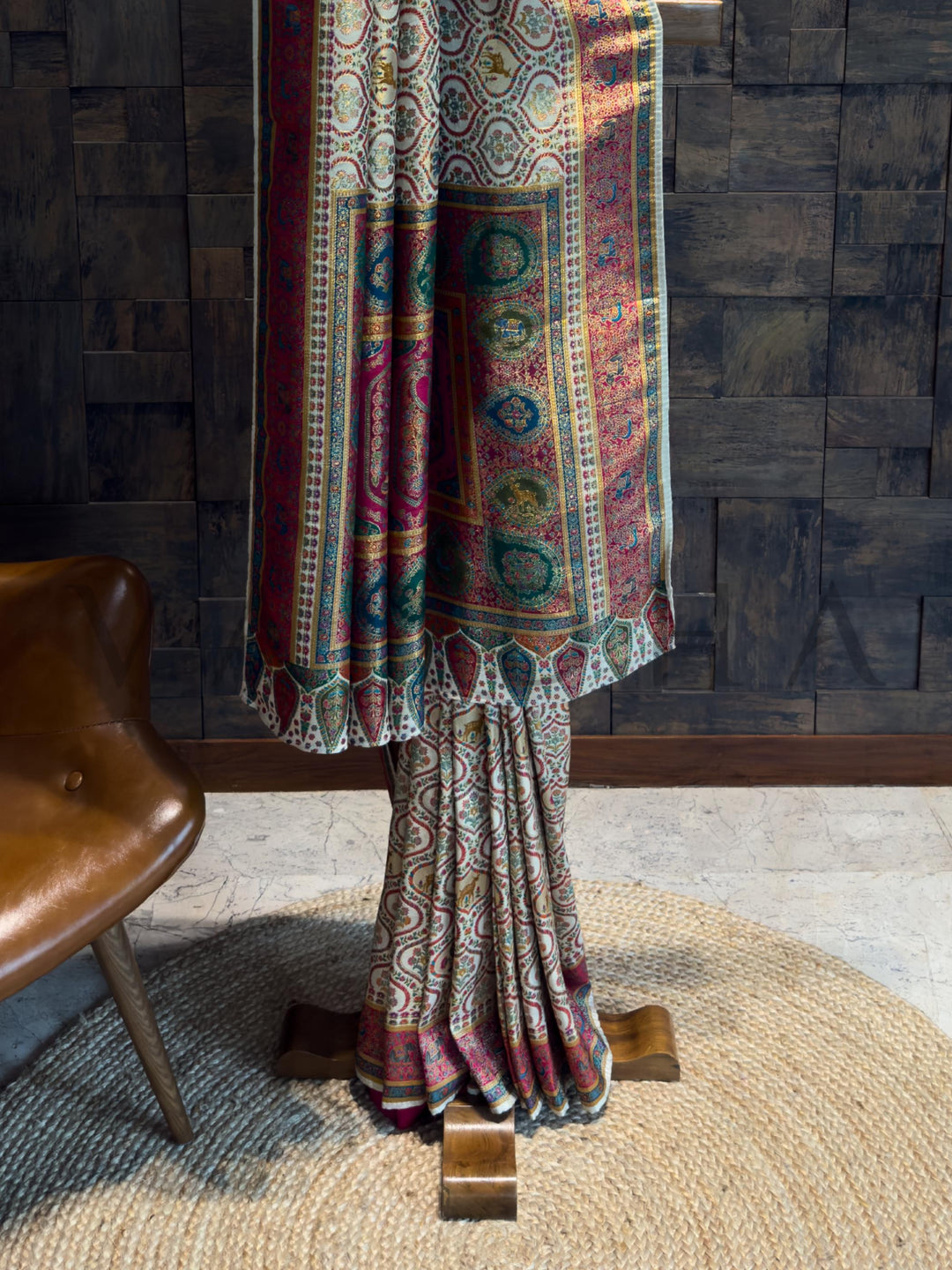 Colorful saree draped over a wooden stand against a textured wall.