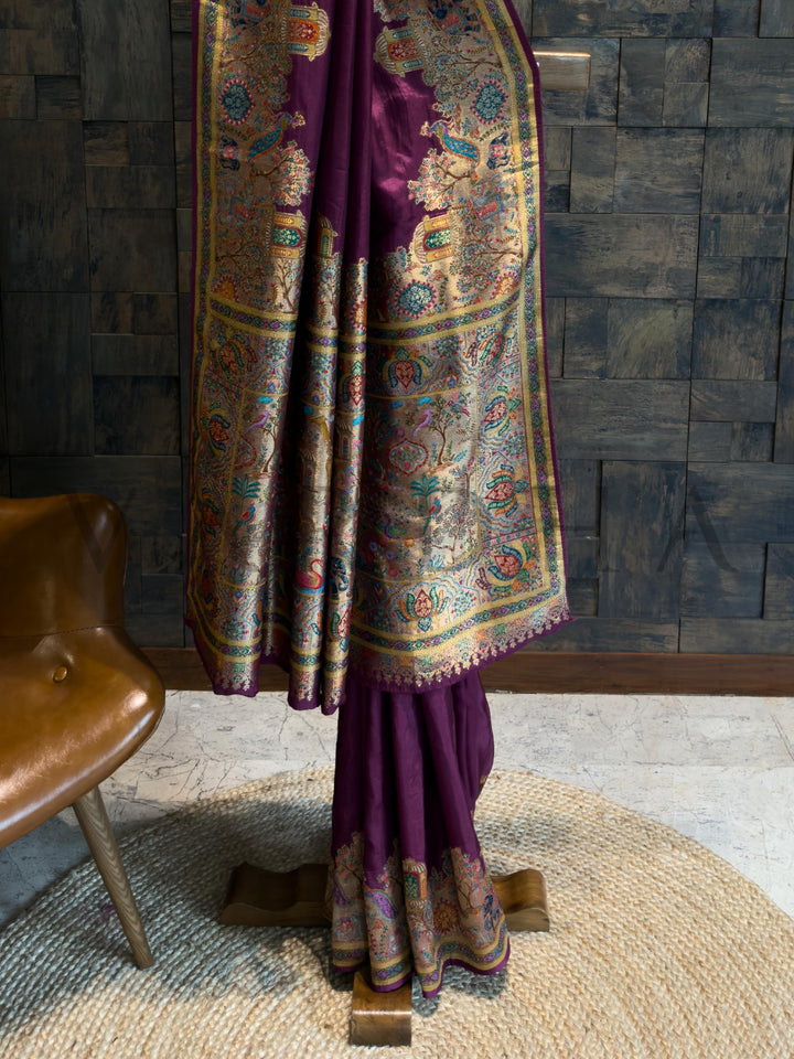 Purple traditional outfit with intricate patterns on a wooden stand against a dark textured wall.