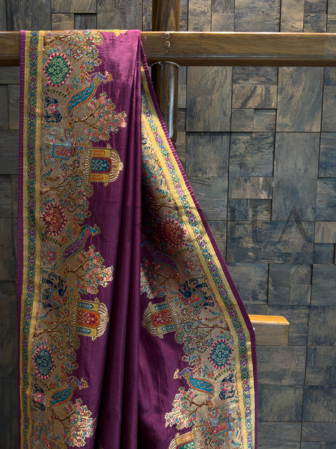 Purple fabric with intricate patterns draped over a wooden rod against a stone wall.