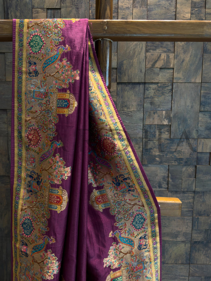 Purple fabric with intricate patterns draped over a wooden rod against a stone wall.