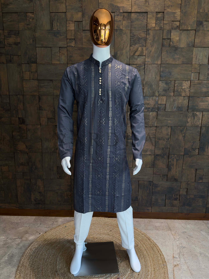 Mannequin wearing a dark gray kurta with intricate patterns against a wooden paneled wall. Charcoal grey viscose men’s kurta with vertical jacquard weaving, subtle sequins, and mandarin collar displayed on mannequin for festive ethnic wear.