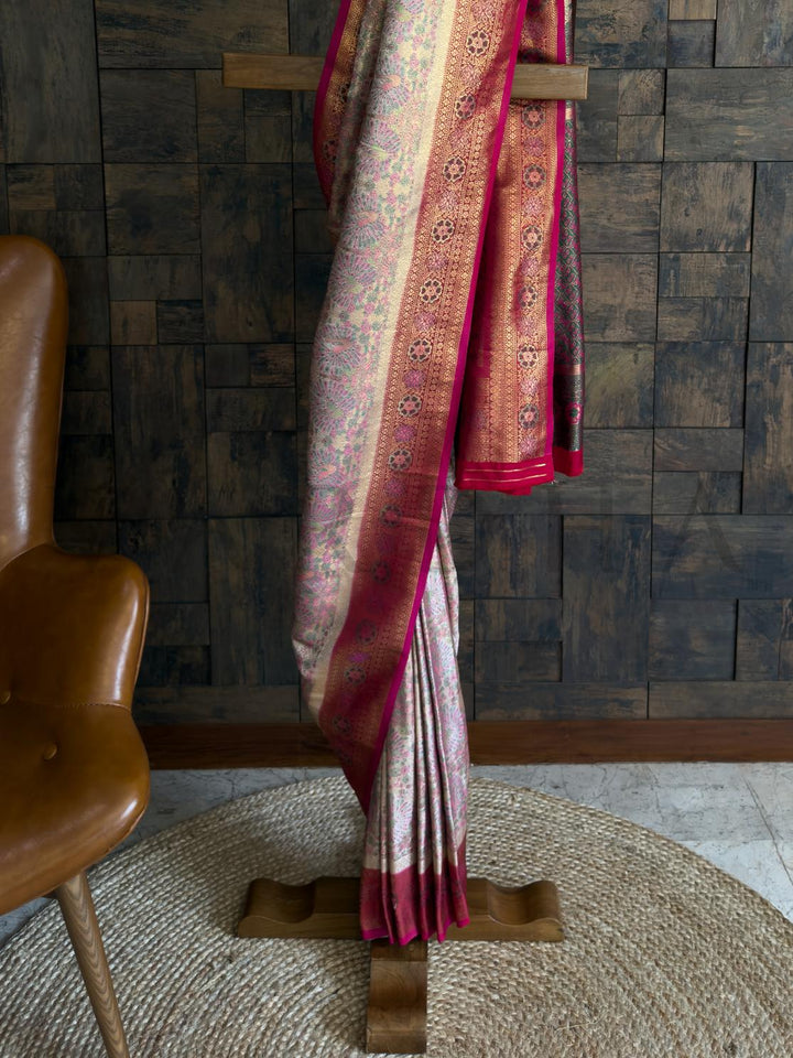 Designer art silk saree in pastel cream with vibrant pink and gold pallu border. Artistic kalamkari saree in cream with floral peacocks and gold zari accents
