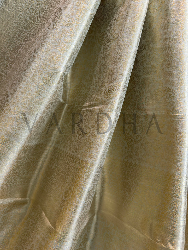 Close-up of champagne tissue saree showing woven floral vines and paisley motifs with metallic sheen, minimal border.