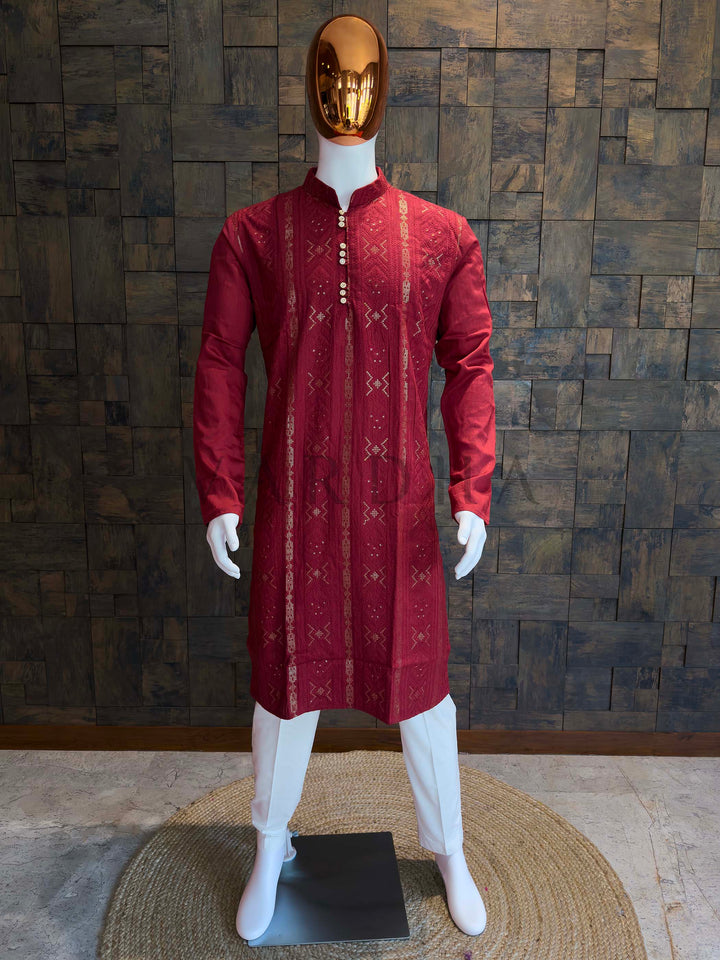 Red kurta on a white mannequin against a wooden paneled wall. Crimson red viscose men’s kurta with vertical jacquard weave, subtle sequins, mandarin collar and gold-tone buttons displayed on mannequin for festive wear.