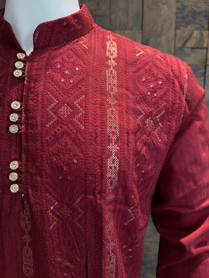 Maroon embroidered garment on a wooden background Close view of stand collar and button placket on crimson jacquard kurta showing raised geometric texture and sparkling sequin pinpoints.
