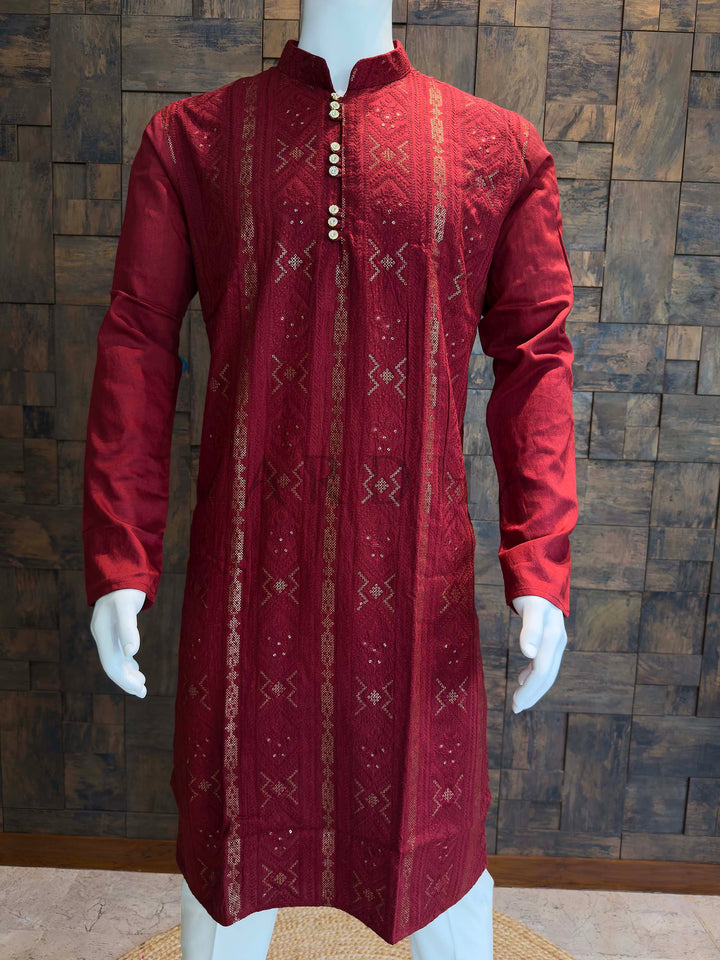 Red embroidered kurta on a mannequin against a wooden paneled wall. Ethnic menswear kurta in deep red with ornate buttons and vertical patterned weave, ideal for festive nights and traditional ceremonies.