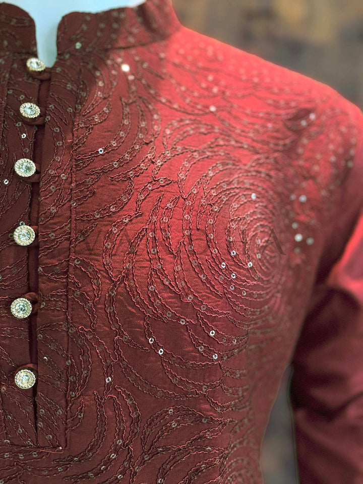 Close-up of a red embroidered garment with intricate patterns and button details. Angled chest view highlighting shimmering rosette patterns in fine sequins with a clean button placket and tailored collar for wedding functions.