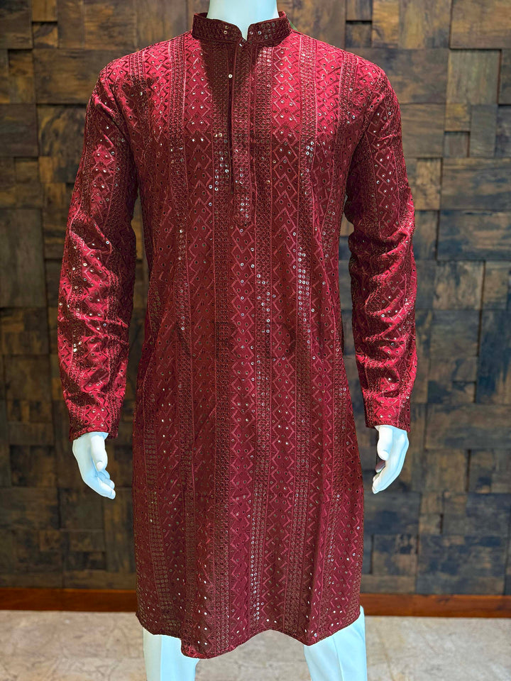 Red velvet kurta on a mannequin against a textured wall. Full-length shot of sequin-embellished red kurta with long sleeves and curved hem—refined ethnic outfit for receptions and sangeet nights.