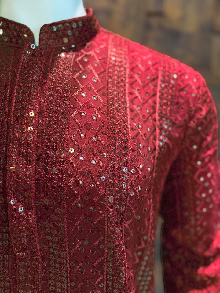 Red embroidered garment on a mannequin with a blurred background Angled chest view emphasizing sequin-trimmed collar, minimalist concealed placket and continuous embellished panels across the body.