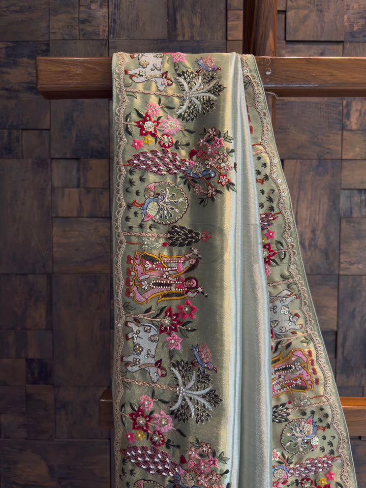 Pista green–gold tissue silk saree drape with narrative embroidery panels and scalloped edge; perfect for party-wear and reception styling.