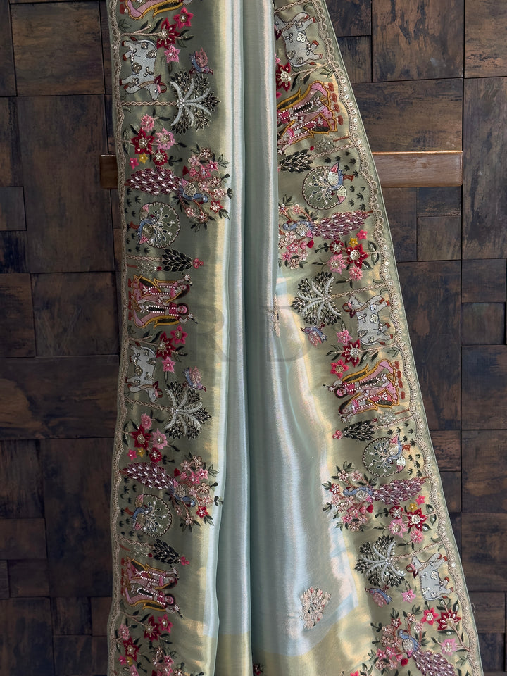 Peacock and floral embroidery with mirrors and stones on luminous tissue base; detailed craftsmanship on turquoise saree border.