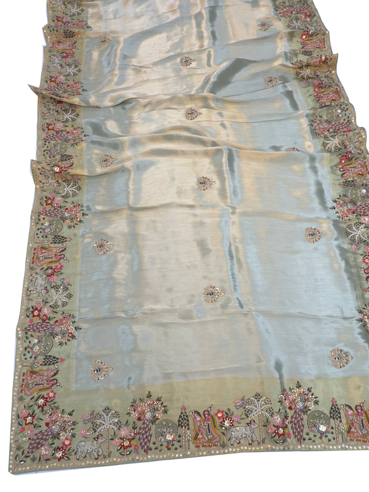 Border embroidery in dusty green saree showing sacred cow, palm trees, peacocks, and sequined blossoms—ideal for spiritual events.