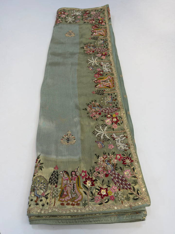 Radha Krishna border theme complemented by light zari shimmer on green silk body—styled for festive gifting or ritual wear.