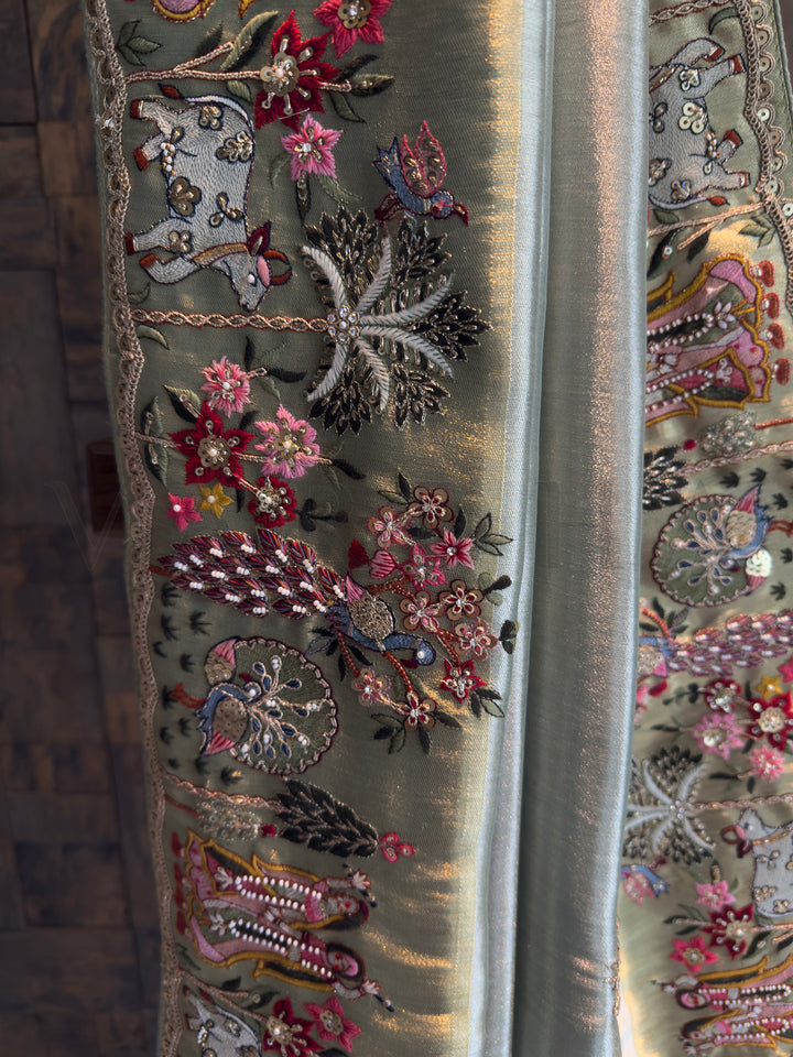 Close-up of embellished border on pista green tissue saree showing mirror accents, sequins, zari and peacock motifs for festive sangeet-ready look.