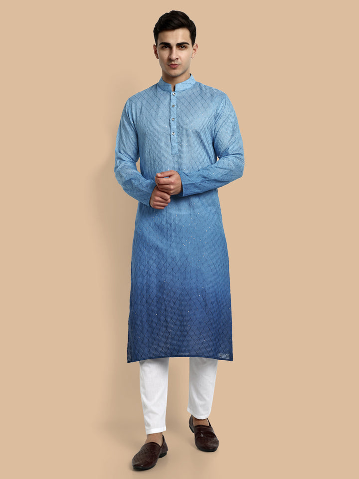 A man wearing a blue cotton kurta with mandarin collar and embroidered details, paired with white trousers. Fusion blue men’s cotton kurta with chikankari embroidery and subtle sequin detailing for festive wear