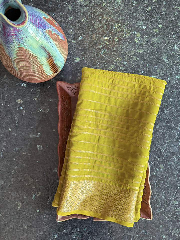 Folded green georgette saree with golden zari striped motifs and border, perfect for haldi, temple wear, and gifting