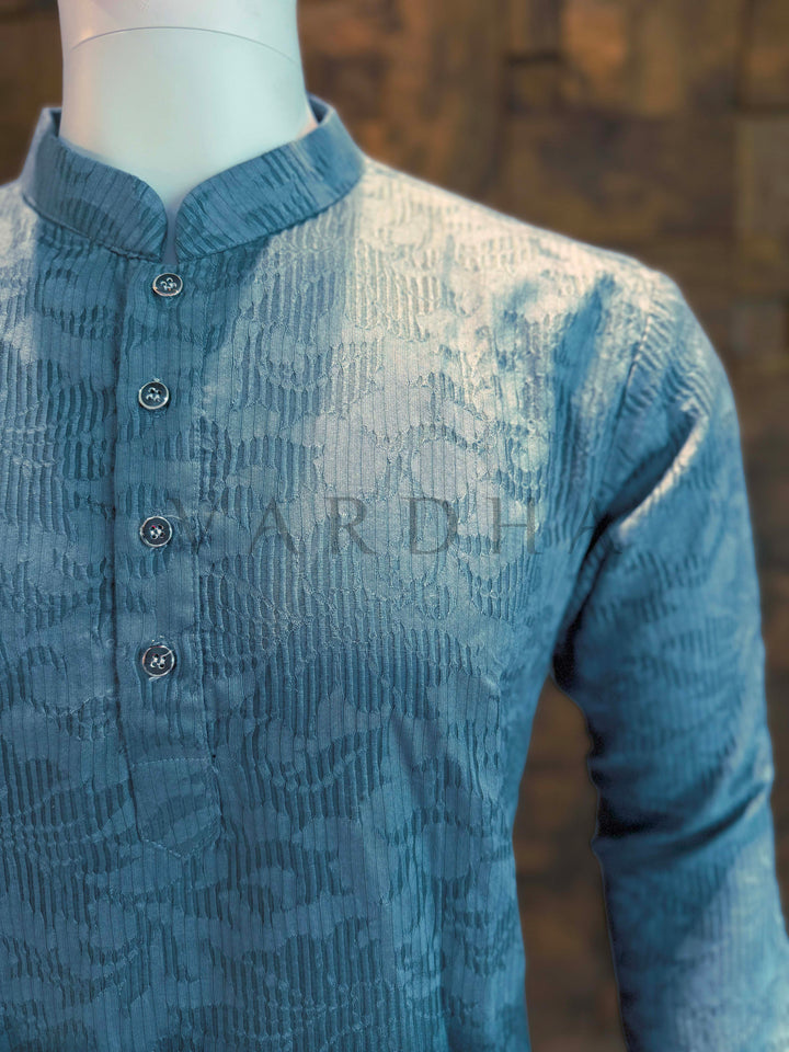 Blue textured shirt on a mannequin with a blurred background Close-up of teal ombré kurta neckline showing mandarin band collar, clean button placket and fine ribbed jacquard weave for elegant festive menswear.