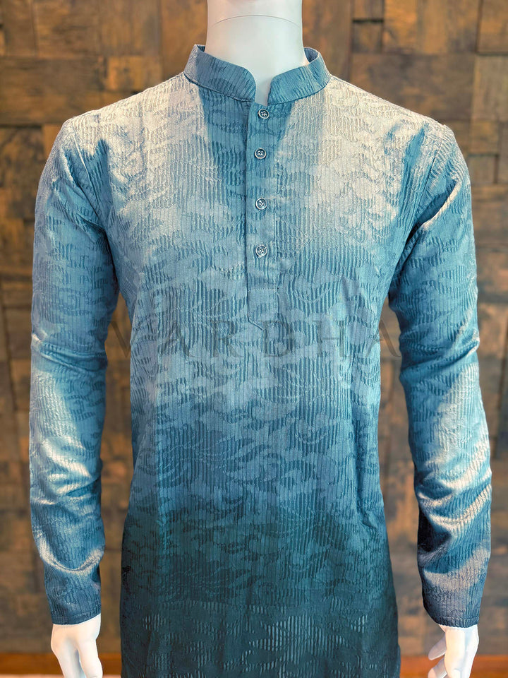 Blue textured shirt on a mannequin against a wooden paneled wall. Front panel detail of viscose kurta highlighting tonal woven texture and gradient from light teal to dark teal/charcoal for modern ethnic style.