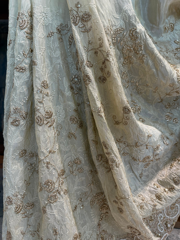 Close-up of embroidered fabric with intricate patterns on a plain background. Ivory Tissue Silk Saree with Hand Zardozi, Sequins, Stone Embroidery & Scallop Detailing