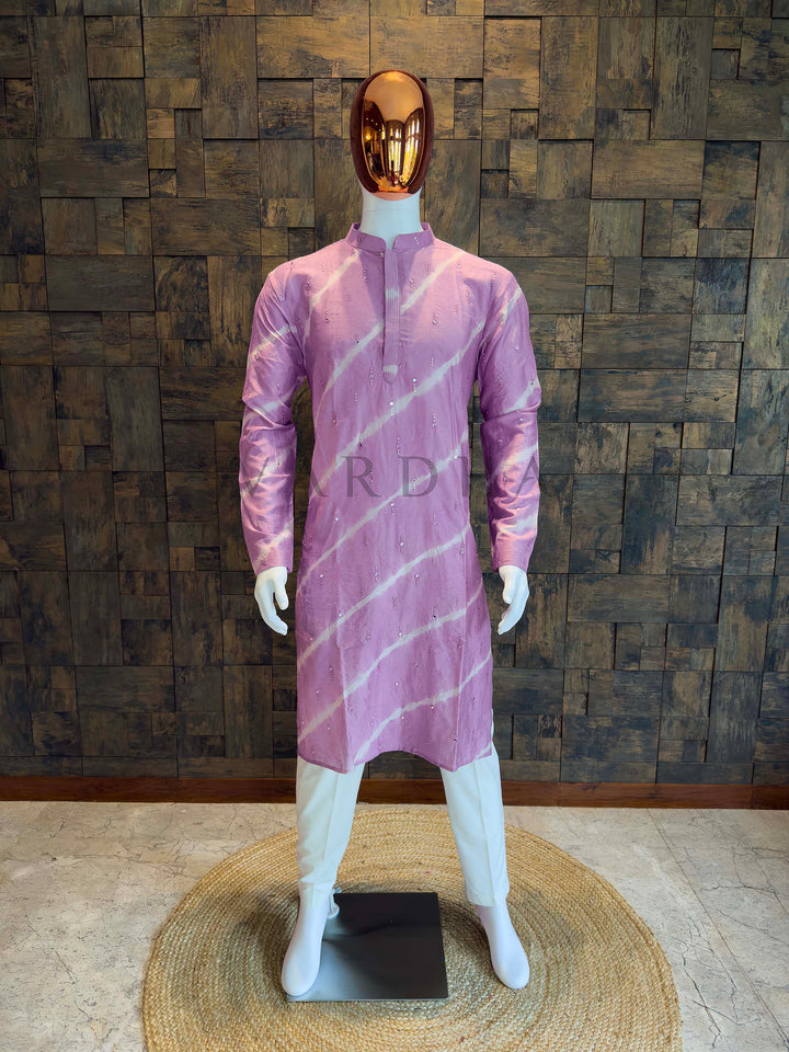 Mannequin wearing a pink kurta with white patterns against a wooden paneled wall. Lilac viscose men’s kurta with mandarin collar, concealed placket and diagonal tie-dye bands accented by scattered sequins, styled with white churidar for festive wear.