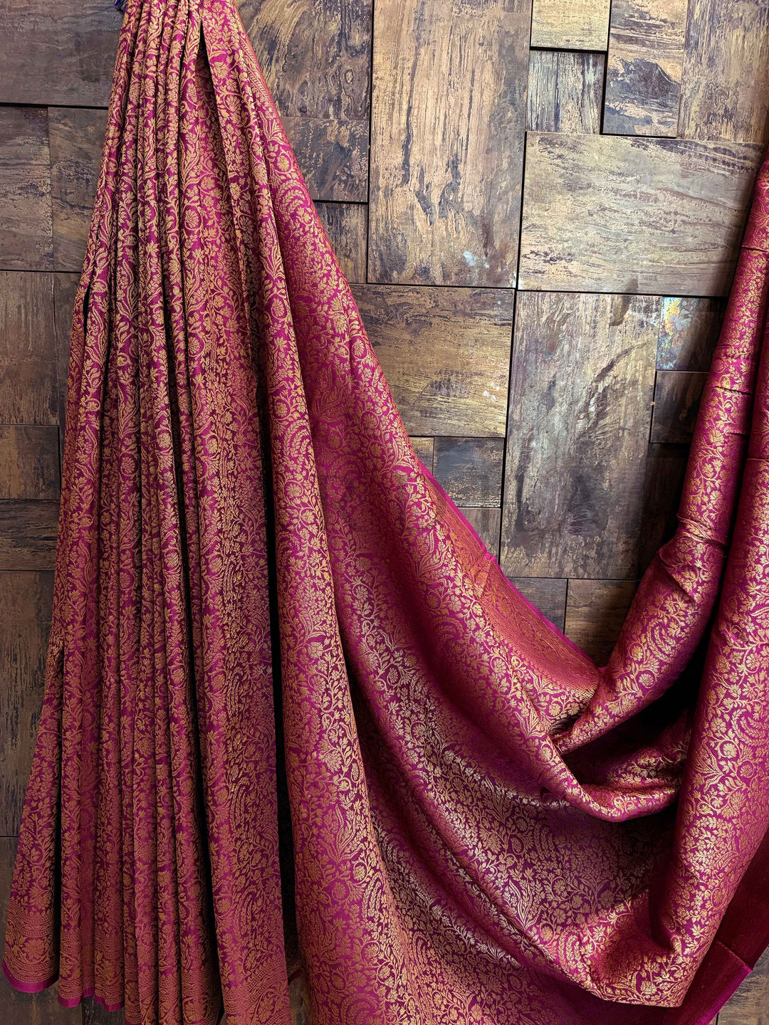 Red patterned fabric draped over a wooden surface Detailed close-up of pallu motifs with mango and latticework intricacies in gold zari over wine background