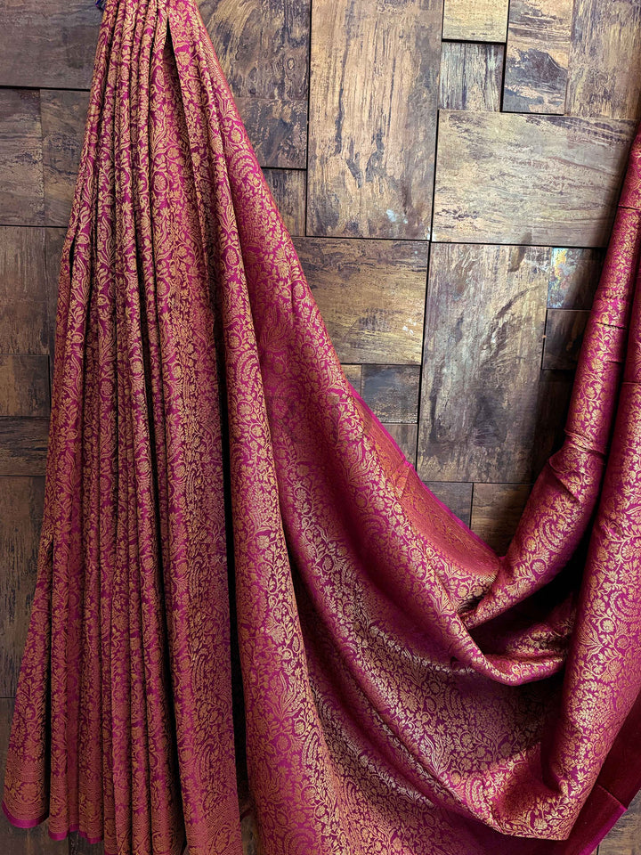 Red patterned fabric draped over a wooden surface Detailed close-up of pallu motifs with mango and latticework intricacies in gold zari over wine background