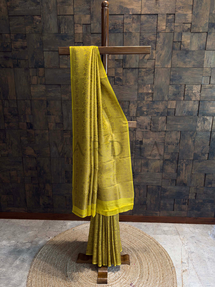 Yellow saree draped over a wooden stand against a textured wall. Mustard yellow Mysore silk saree with golden zari weaving and animal-floral motifs displayed elegantly on a wooden stand.