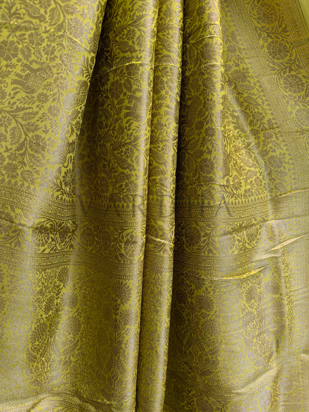 Close-up of green fabric with intricate patterns Border view of mustard yellow Mysore silk saree featuring symmetric floral patterns in zari.