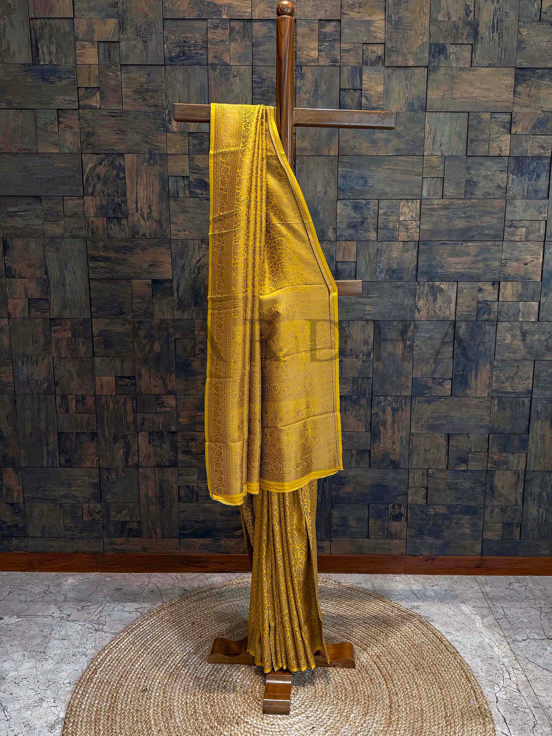 Yellow saree on a wooden hanger against a textured wall. Mustard Gold Mysore Silk Saree with full view drape showing traditional golden zari floral design