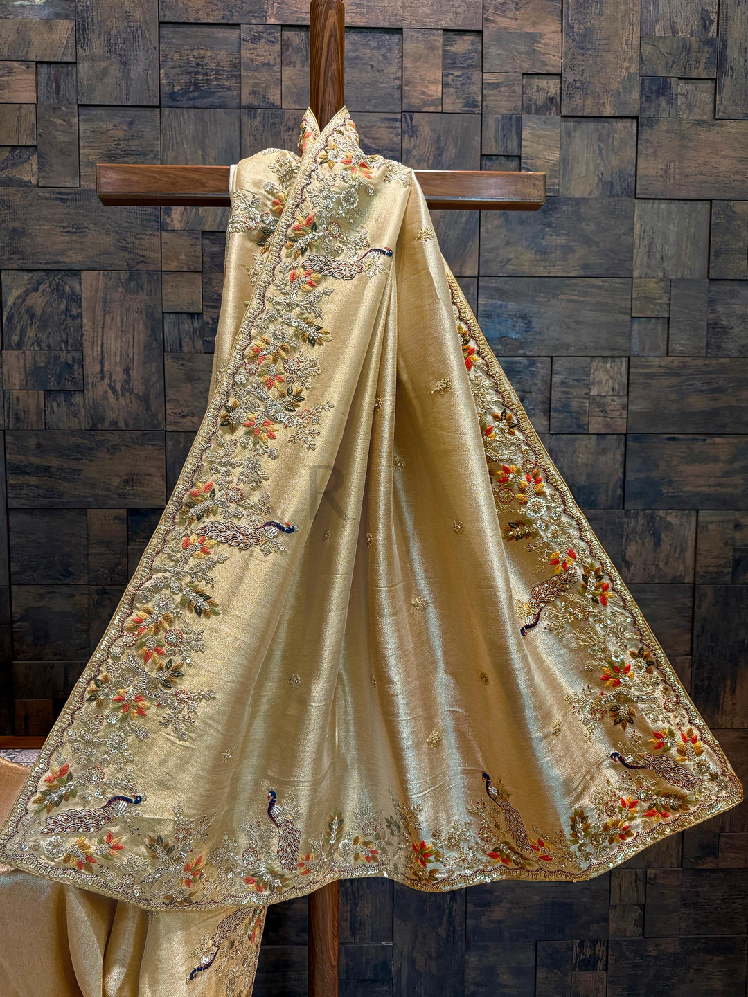 Zoomed image of the zari weaving pattern on the saree base with visible metallic luster and fine thread density. Decorative fabric with intricate embroidery on a wooden background