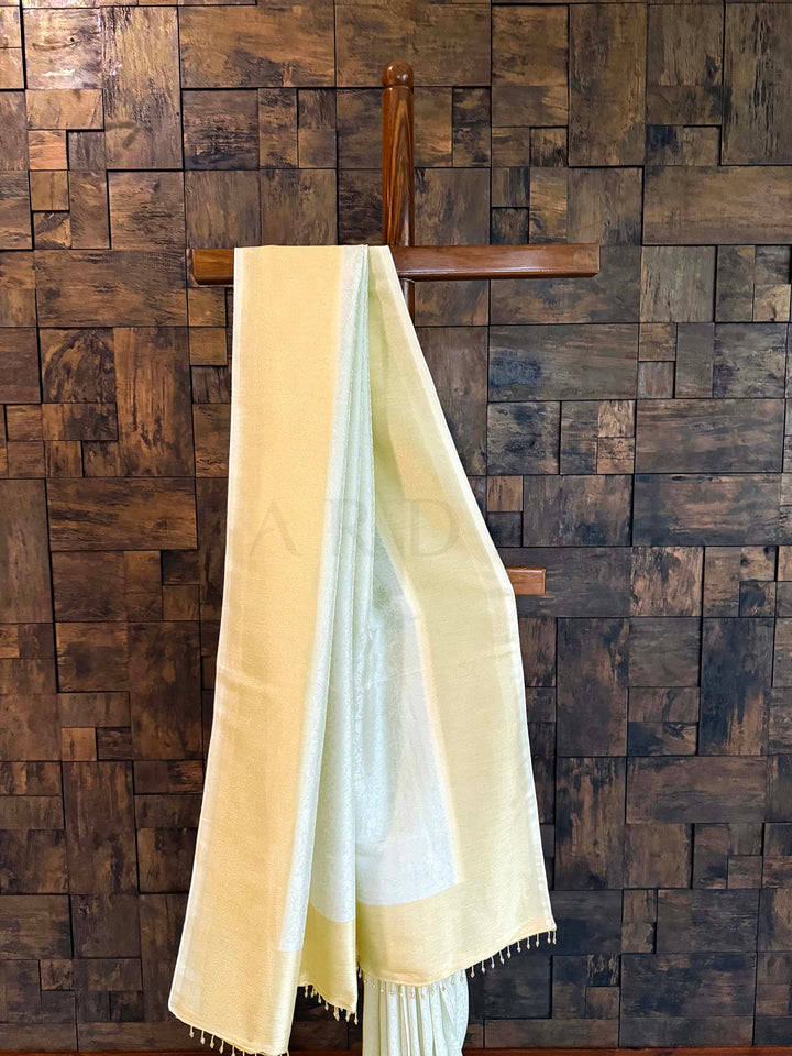 Two scarves draped over a wooden hanger against a wooden paneled wall. Close-up of gold tissue border with pistachio-mint body showing subtle sheen.