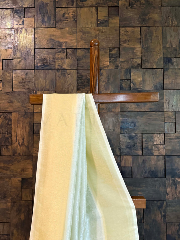 Two scarves hanging on a wooden rack against a wooden paneled wall. Edge view showing lilting tassels and refined zari tissue border.