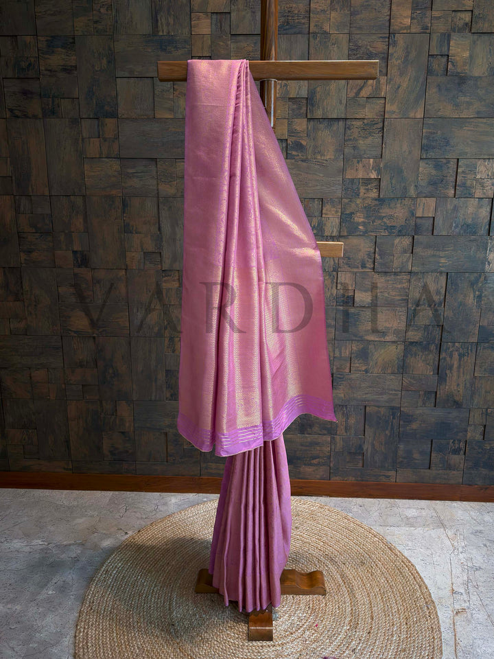 Orchid lavender Kanjivaram art silk saree folded with golden zari floral jaal and geometric brocade border, pastel sheen and traditional craftsmanship visible.