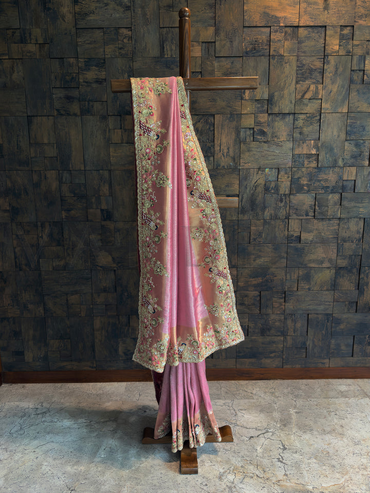 Pink Kanjivaram tissue silk saree with gold undertones and floral-peacock embroidery along scalloped border.