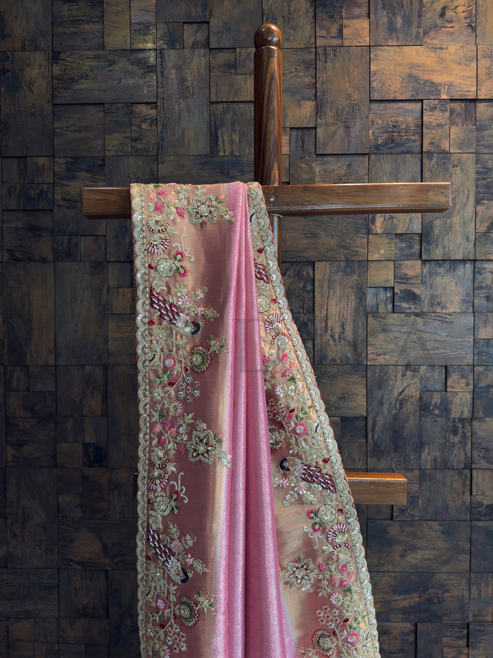 Close-up of pink tissue silk saree featuring zari, sequins, and bead embroidery with peacock motifs.