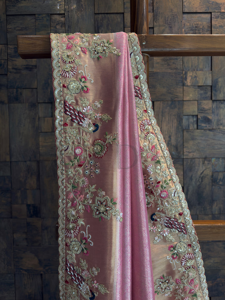Wedding wear pink Kanjivaram tissue saree glowing with gold accents and peacock embroidery.