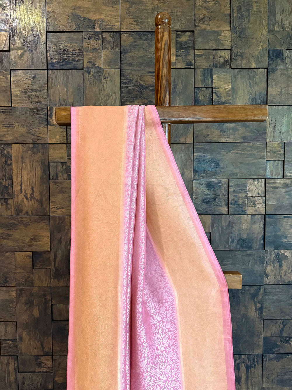 Pink fabric draped over a wooden rod against a stone wall. Close-up of peach-gold tissue border with pink selvedge showing glossy sheen.