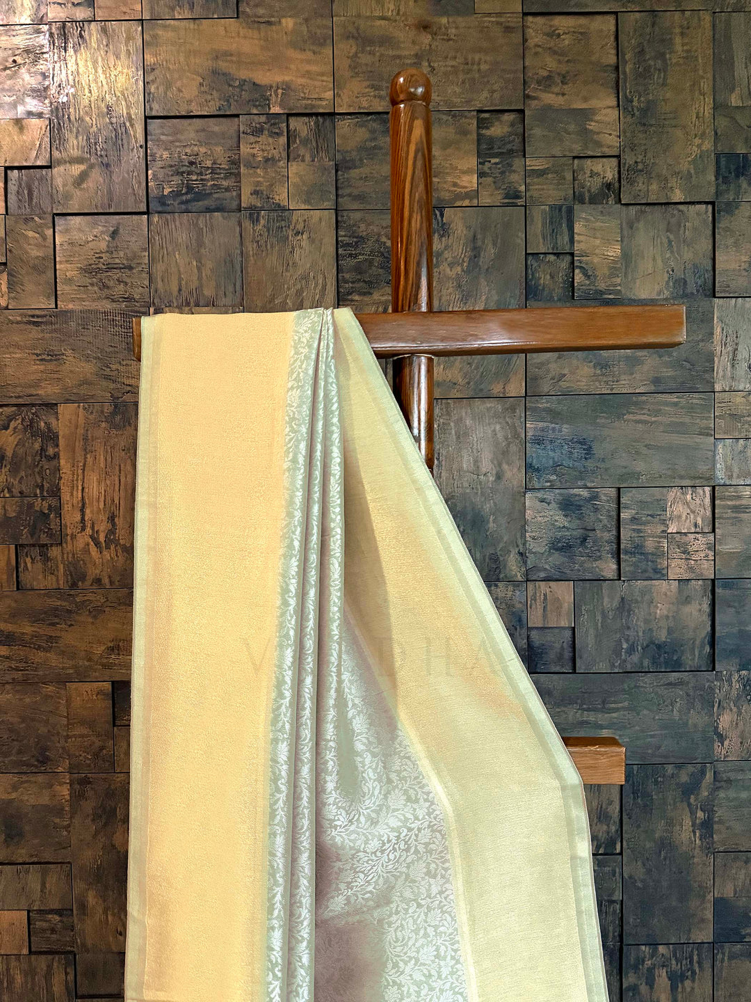 Beige and silver fabric draped over a wooden chair against a wooden paneled wall. Close-up of shimmering tissue border in butter-gold with icy-mint selvedge.