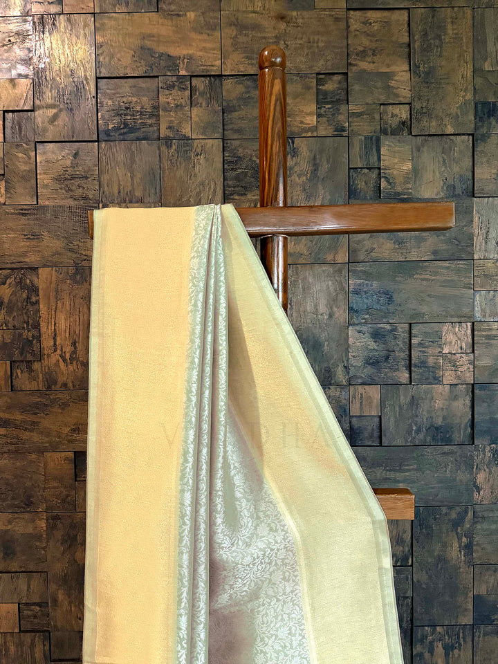 Beige and silver fabric draped over a wooden chair against a wooden paneled wall. Close-up of shimmering tissue border in butter-gold with icy-mint selvedge.