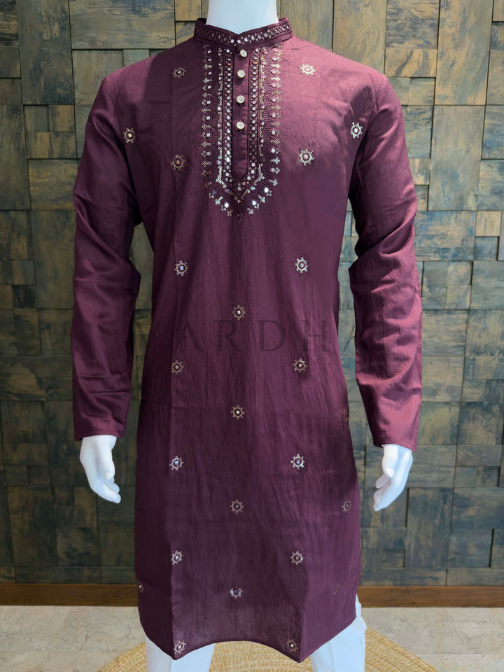 Maroon embroidered kurta on a mannequin against a wooden paneled wall. Front panel detail of men’s plum kurta featuring sheesha work, neat button placket and delicate zari embroidery on smooth viscose fabric with gentle sheen.