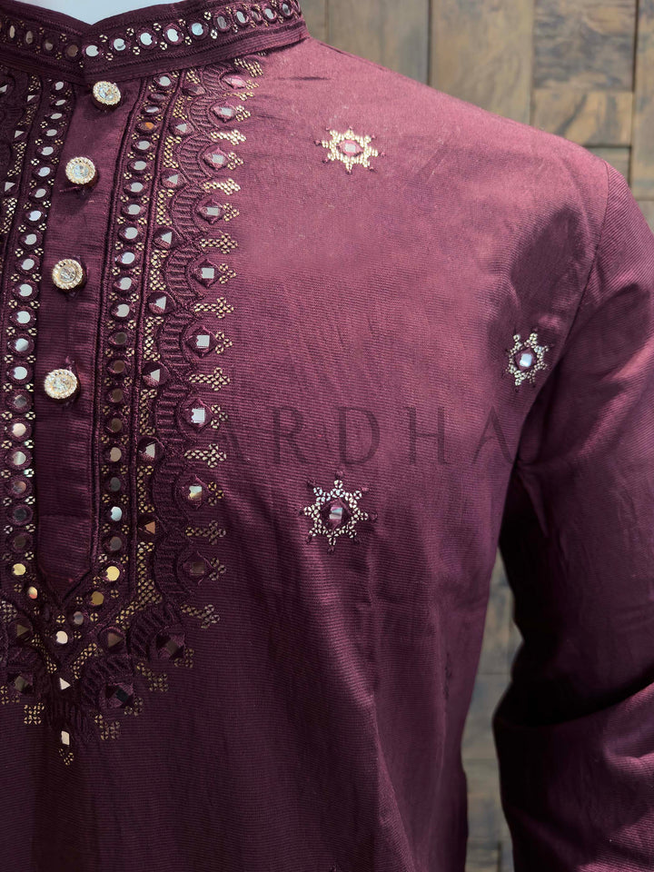 Maroon traditional outfit with intricate embroidery on a wooden background Macro texture of viscose kurta revealing reflective mirrors, fine thread work and zari accents arranged in scalloped motifs around the placket.