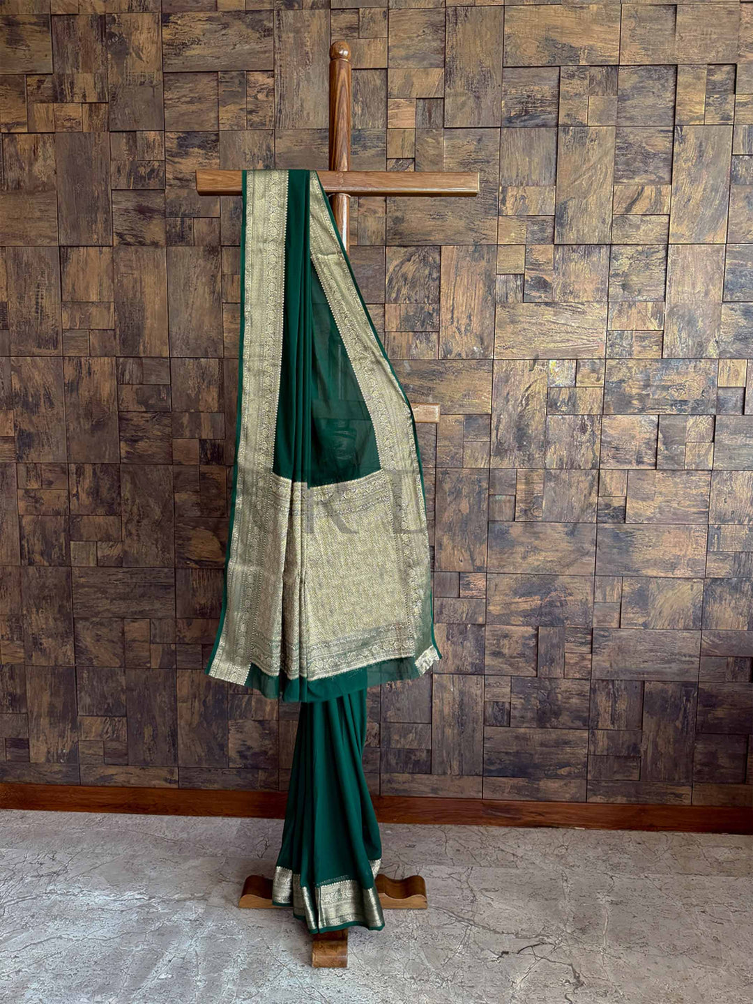 An exquisite emerald green saree in feather-soft georgette, adorned with a finely detailed gold zari border. The saree's fluid texture and rich color make it a standout piece for any occasion.