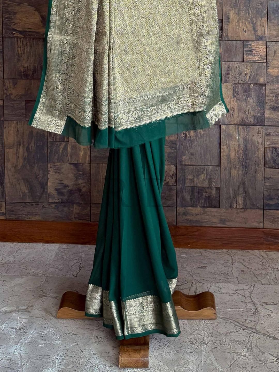 A stunning green georgette saree with delicate gold zari work, artistically arranged to showcase its timeless appeal. The saree’s soft, flowy fabric complements its sophisticated craftsmanship.